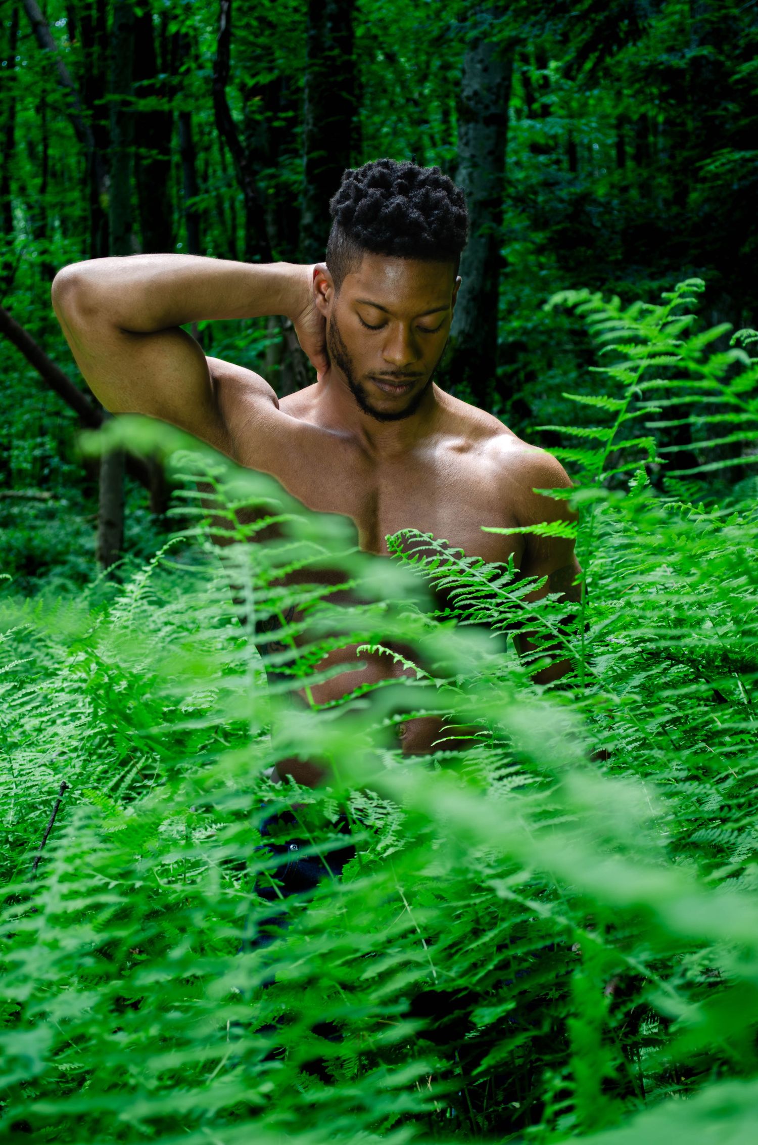 Men's Boudior. Artistic portrait in lush green forest with ferns and trees creating natural framing effect.