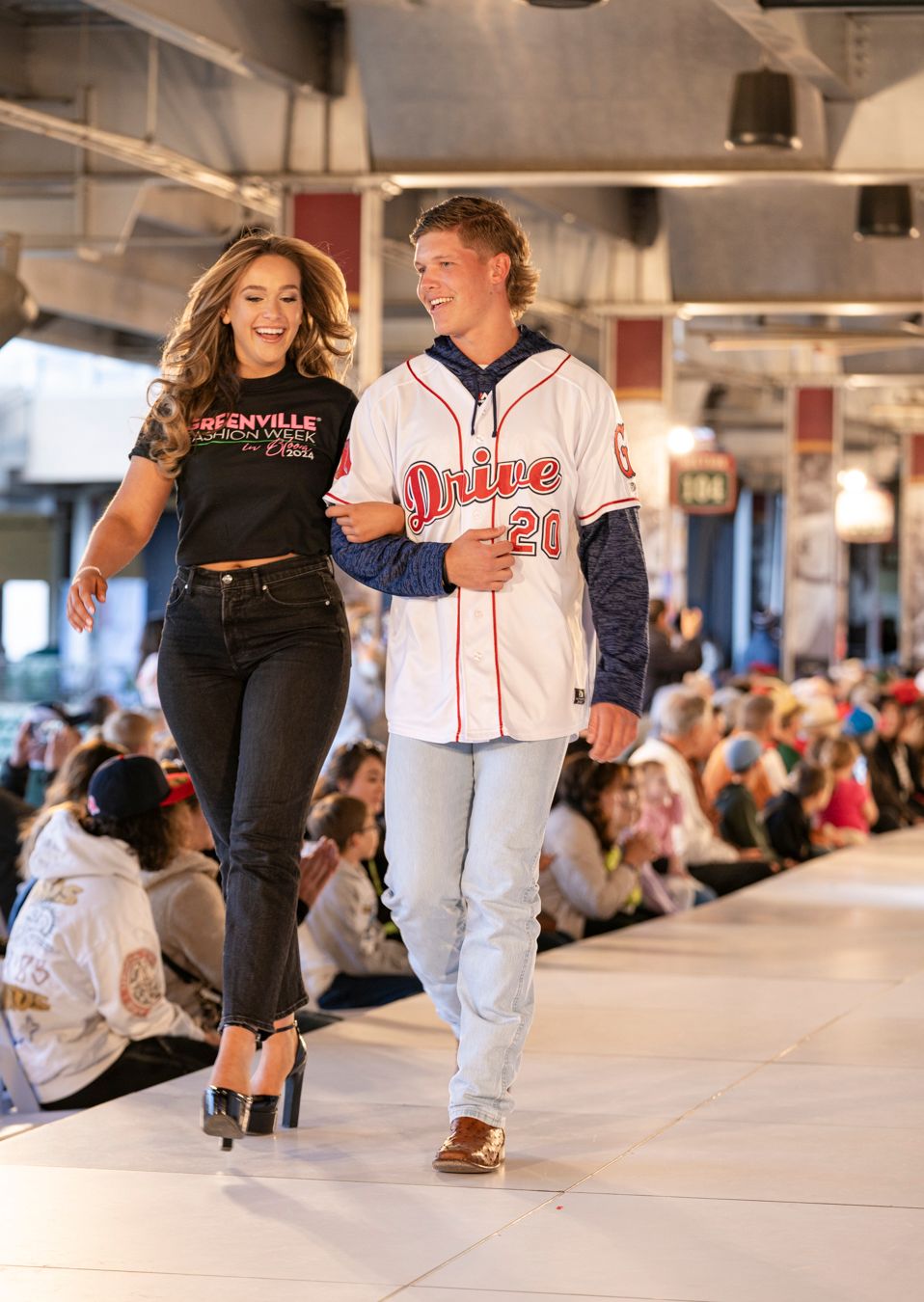 Models walk down a runway wearing casual and baseball-inspired outfits during a fashion show presentation.