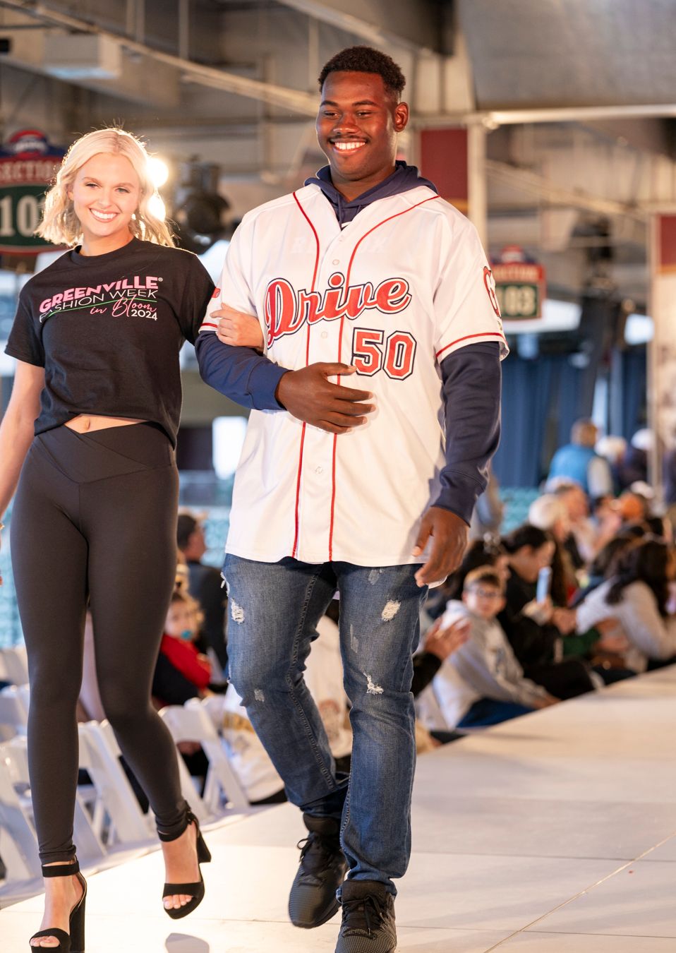 People walking and modeling on a fashion runway in casual and athletic wear at an indoor venue.