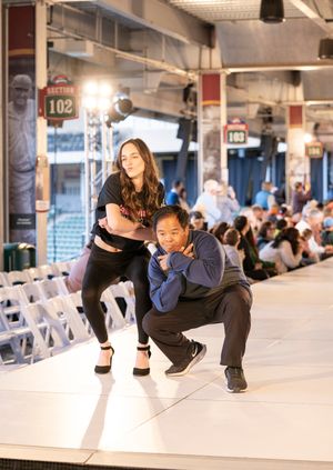 Models posing and walking on a white runway with stadium seating visible in the background.
