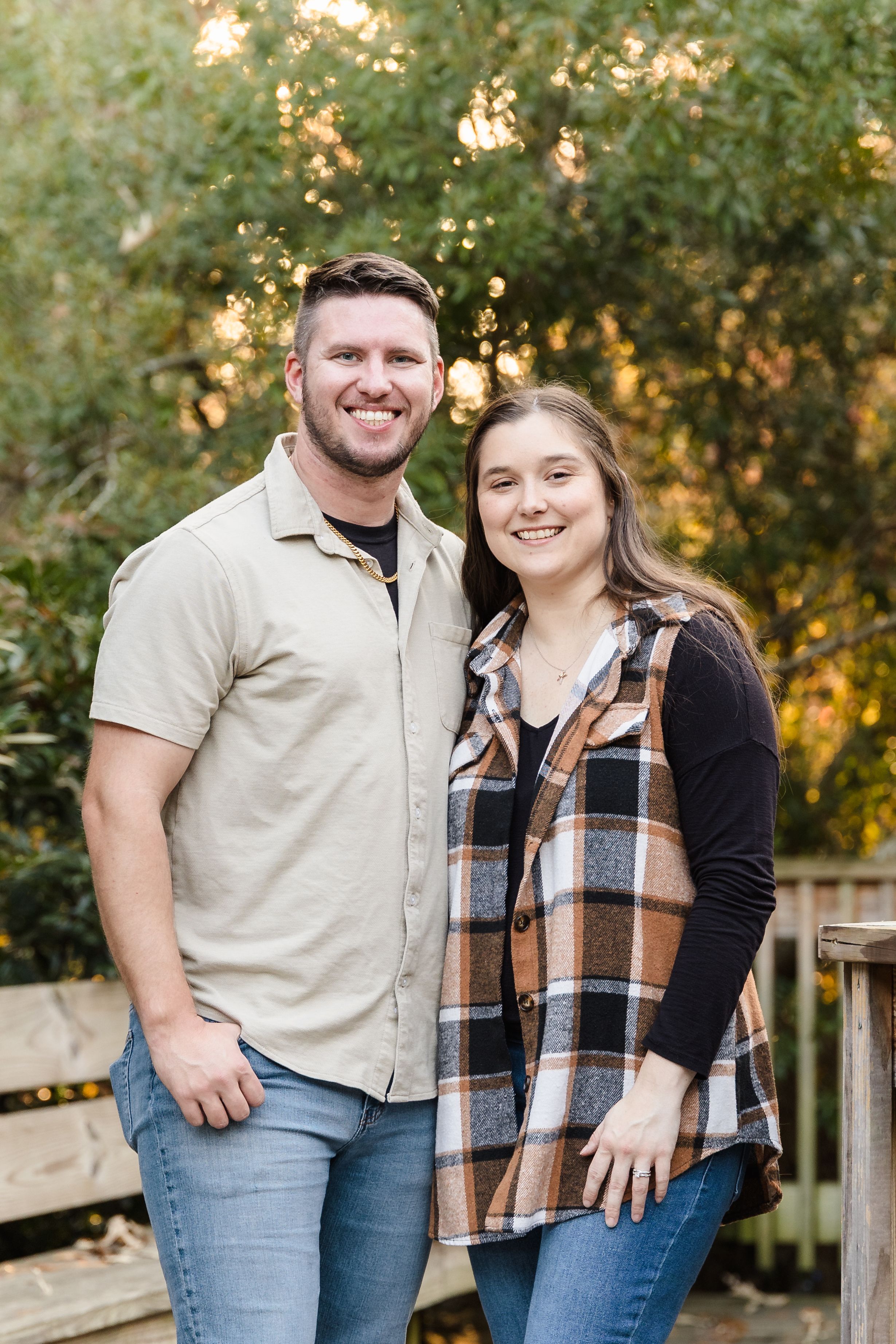 Couple in casual attire poses against autumn foliage background at sunset.