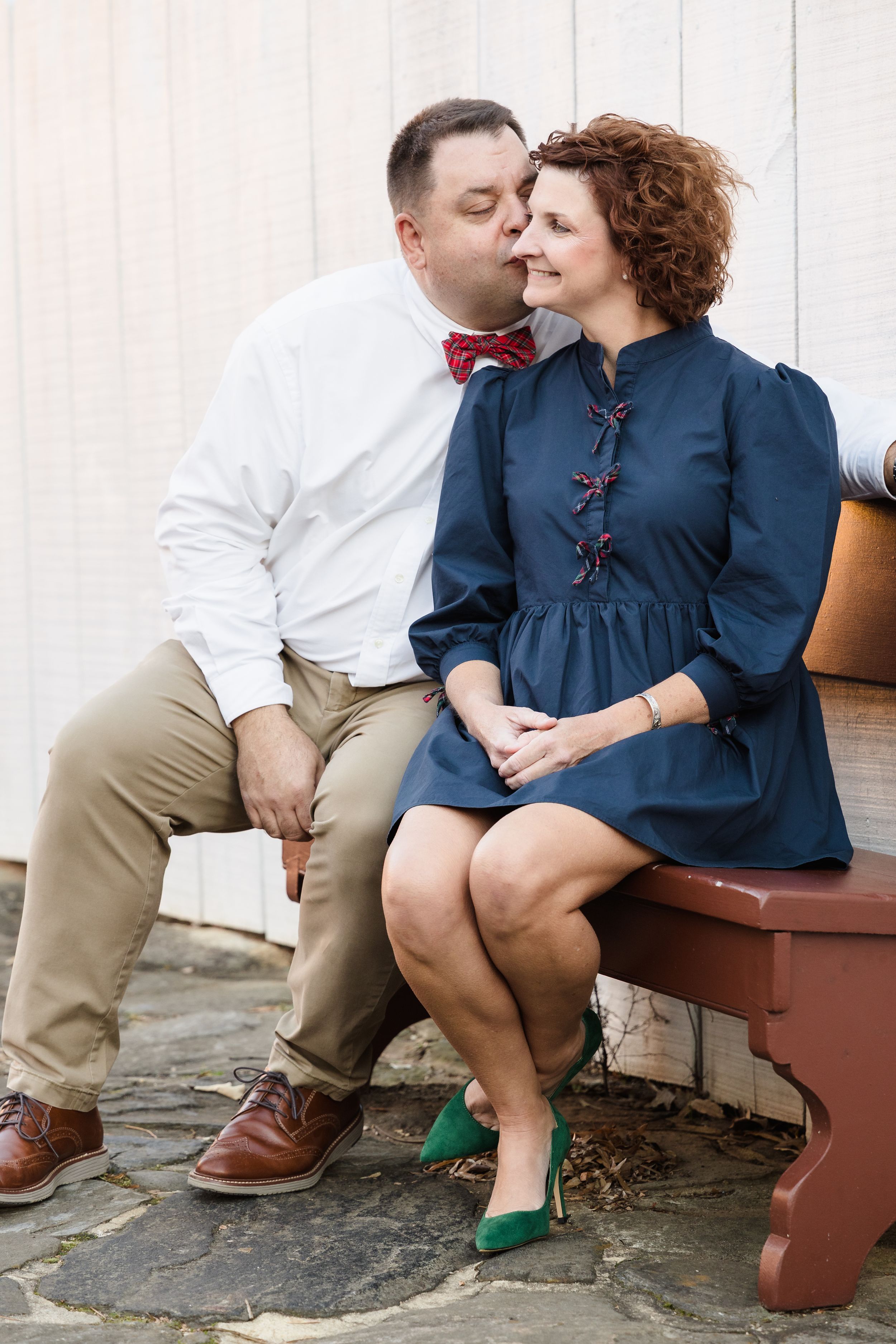 Couple shares intimate moment while sitting on brown bench outdoors.