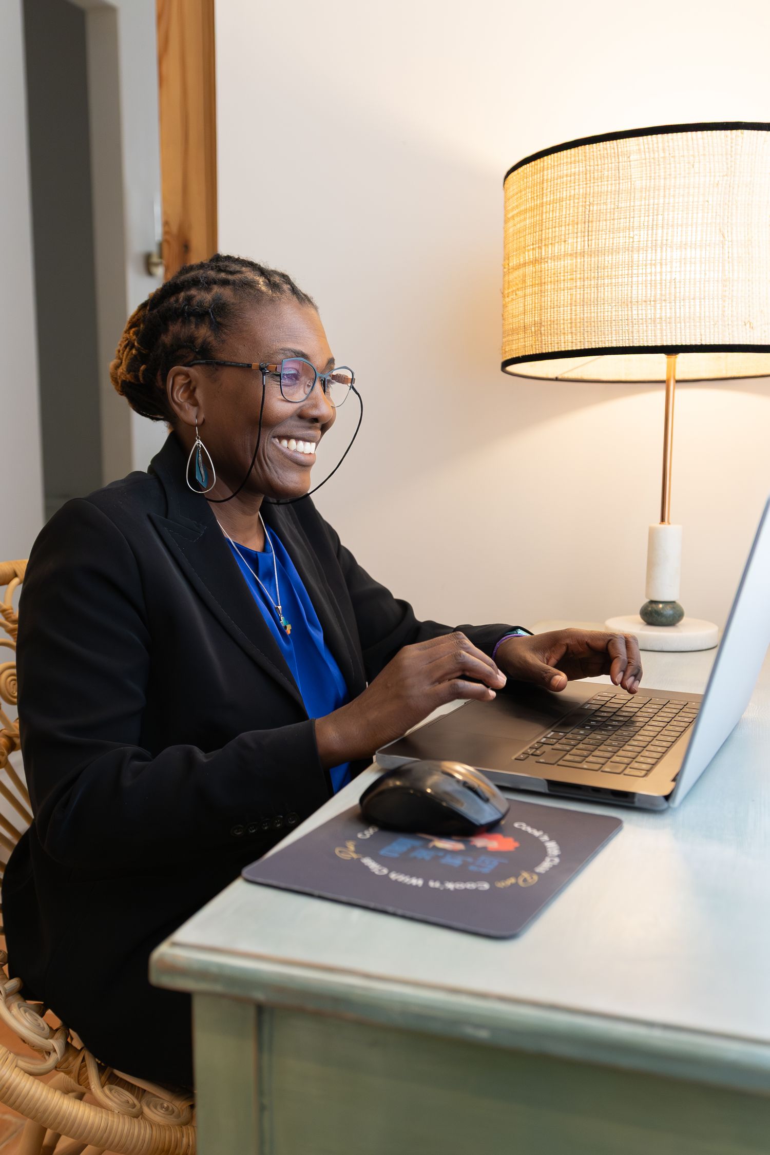 Professional working at desk with laptop and lamp while smiling in a modern office setting.