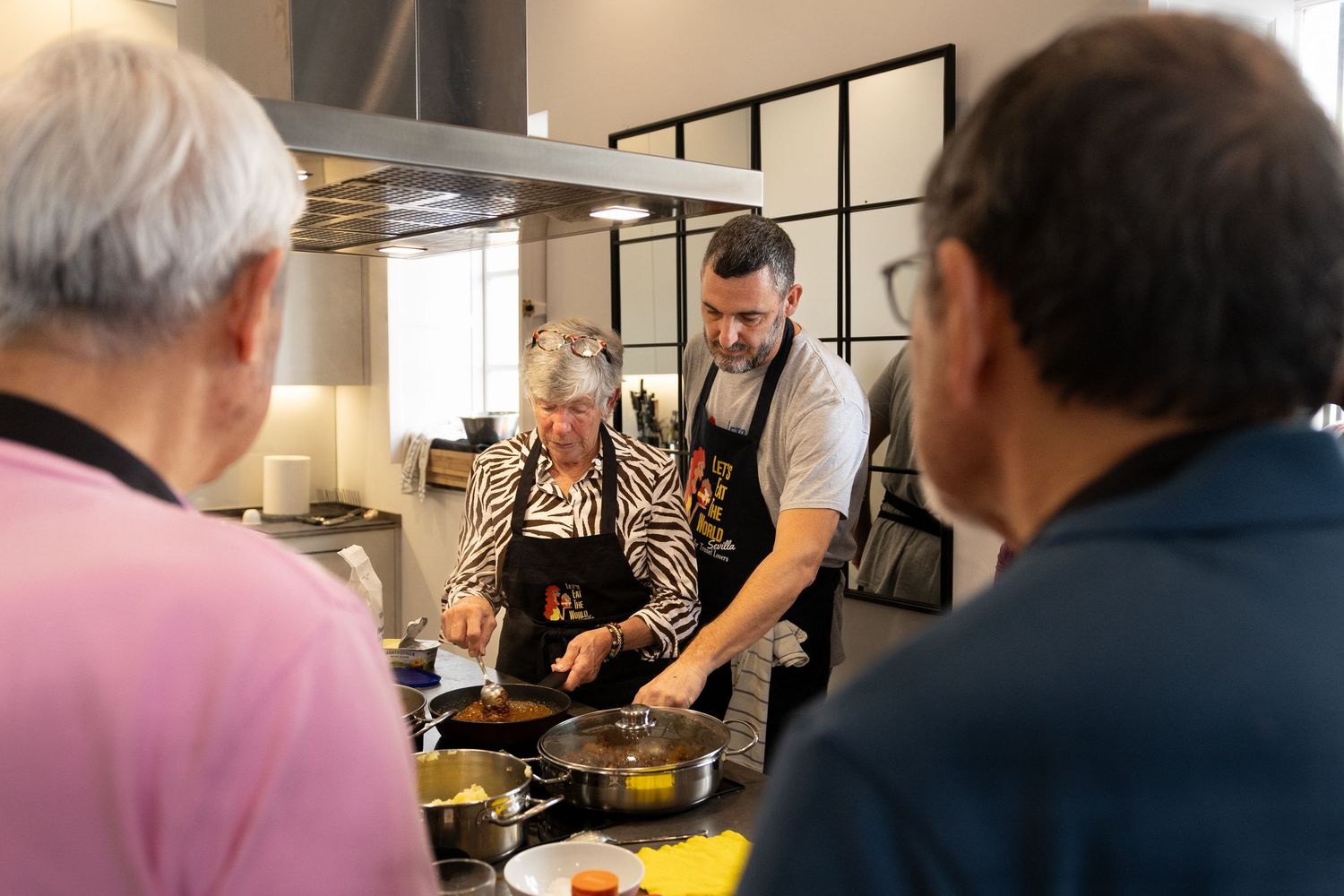 A chef in a restaurant kitchen stirs food in a large pan while other kitchen staff work in the background.
