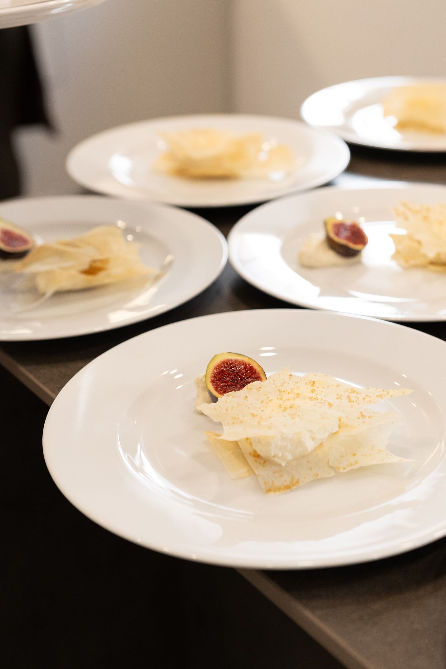 A series of white plates displaying thin slices of parmesan cheese and figs arranged in a restaurant setting.