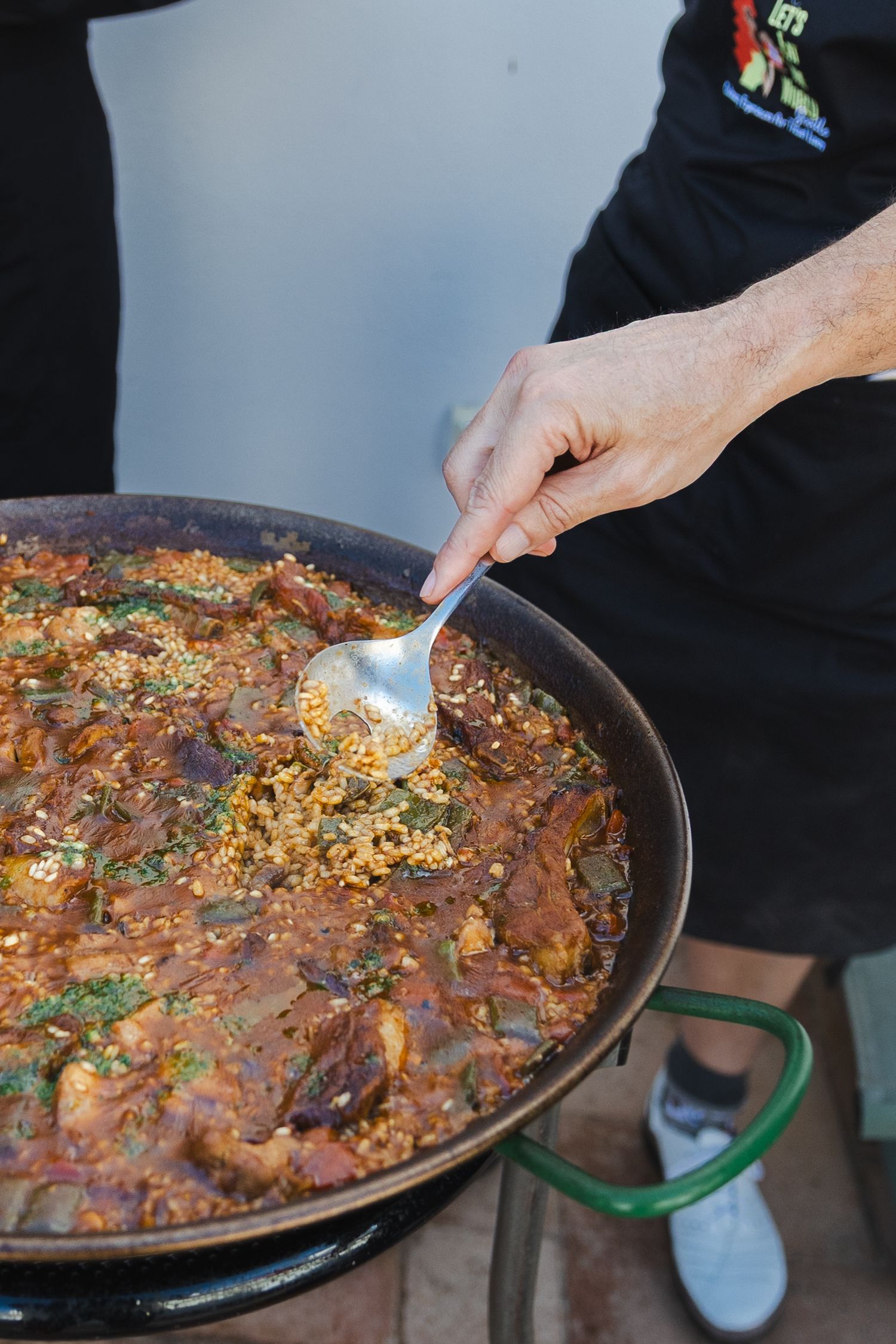 A series of photos showing paella being cooked in a traditional pan with meat, vegetables and seasonings being added.