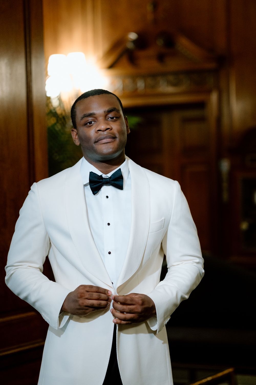 Groom in white tuxedo jacket and black bow tie adjusting his formal wear.
