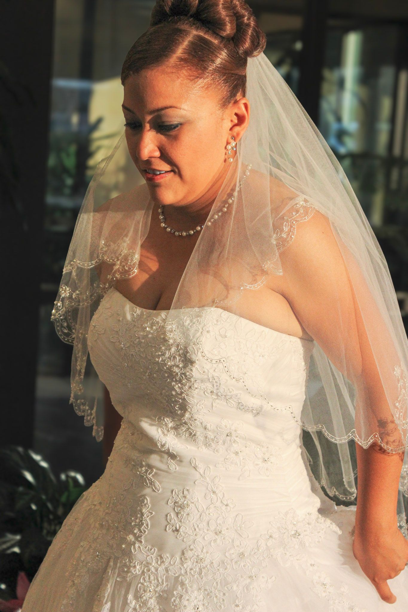 Black and white photo of a bride in a white wedding dress and veil laughing while looking down at her ring.