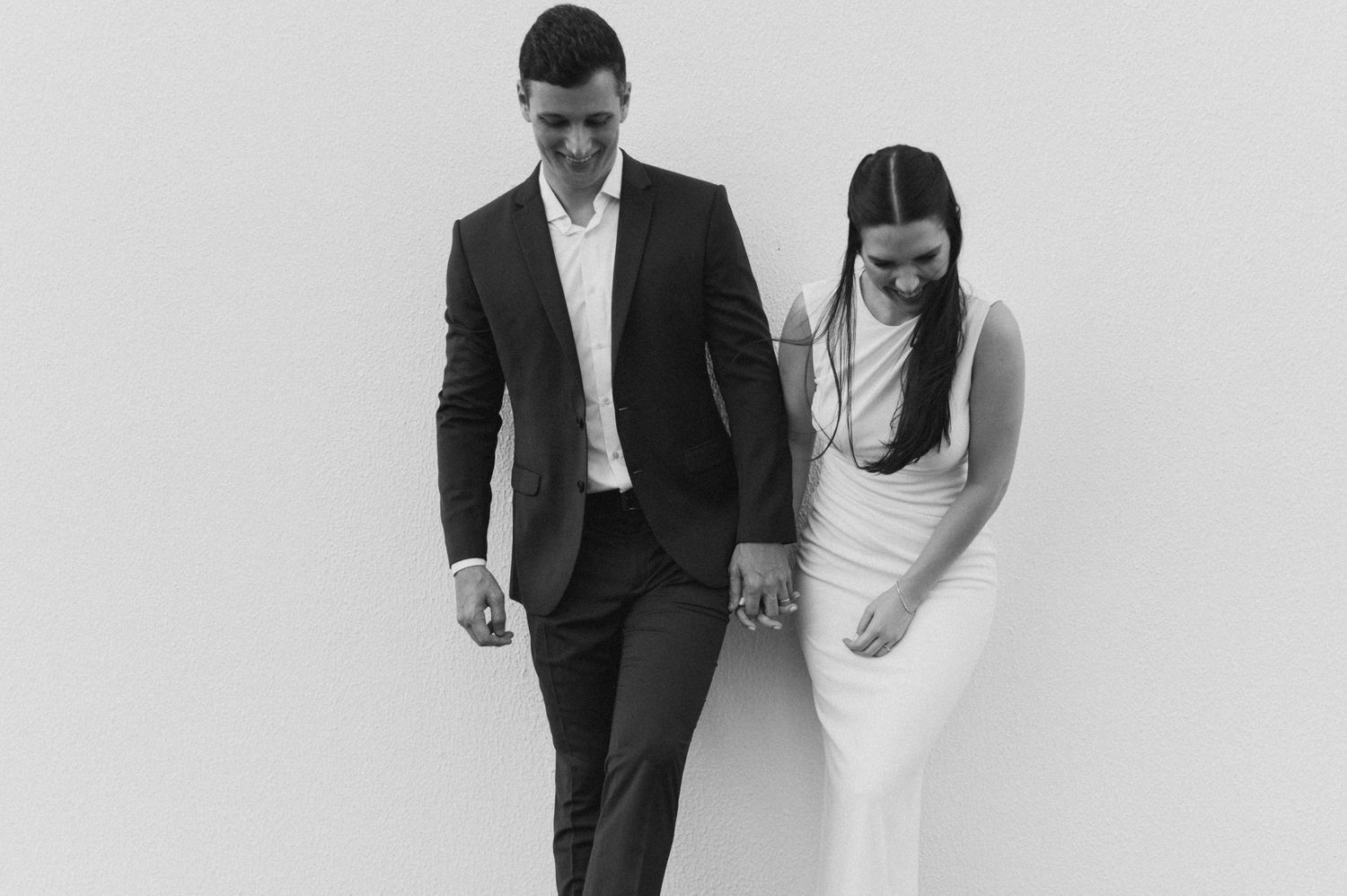 A black and white wedding portrait of a couple posing against a plain wall.