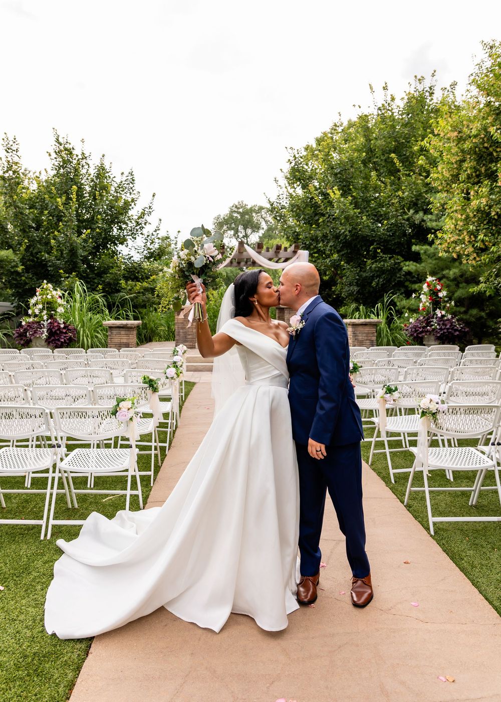 Wedding ceremony setup outdoors with white chairs and floral arrangements on a beautiful summer day.