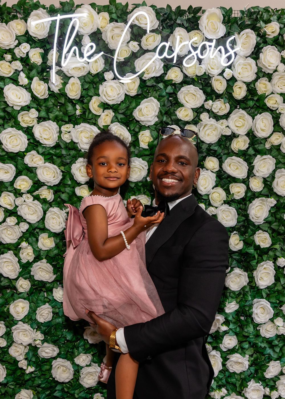 Wedding portraits against a floral wall backdrop with white roses and greenery.