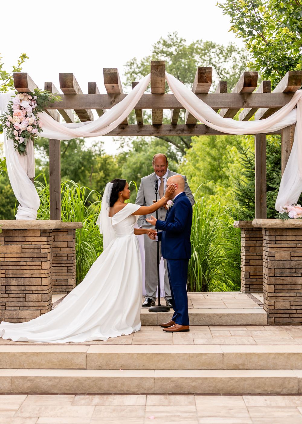 Wedding ceremony under white draped wooden pergola with stone columns at Villa Aletta in Omaha, NE.