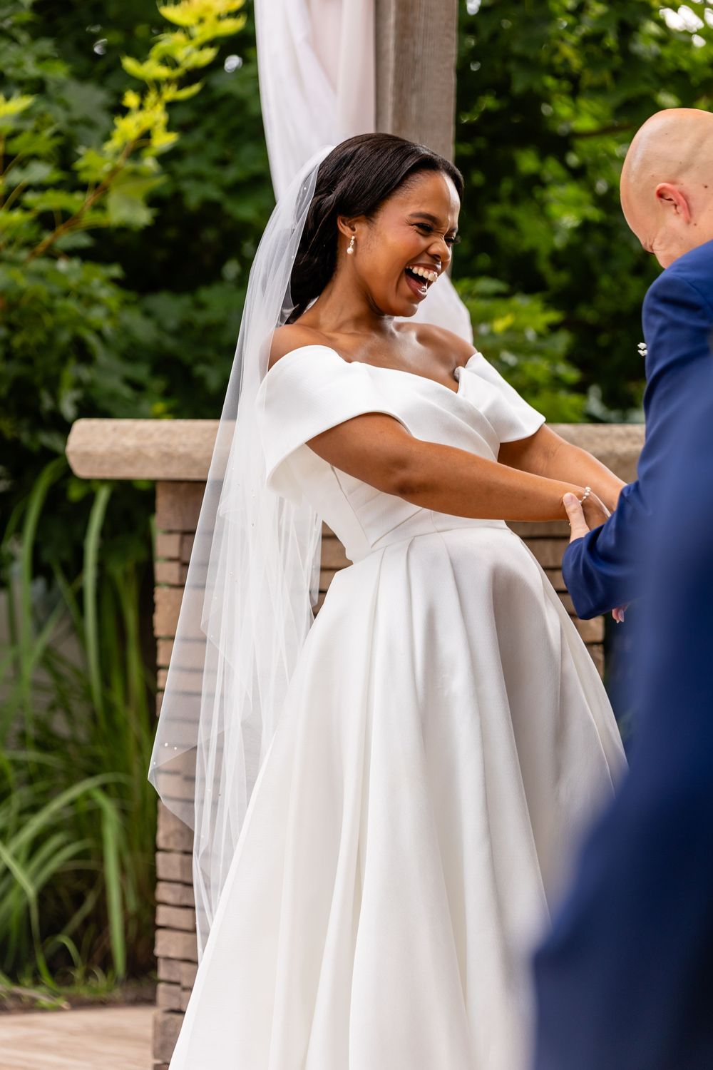 Joyful couple shares a tender moment during their outdoor wedding ceremony under a pergola.