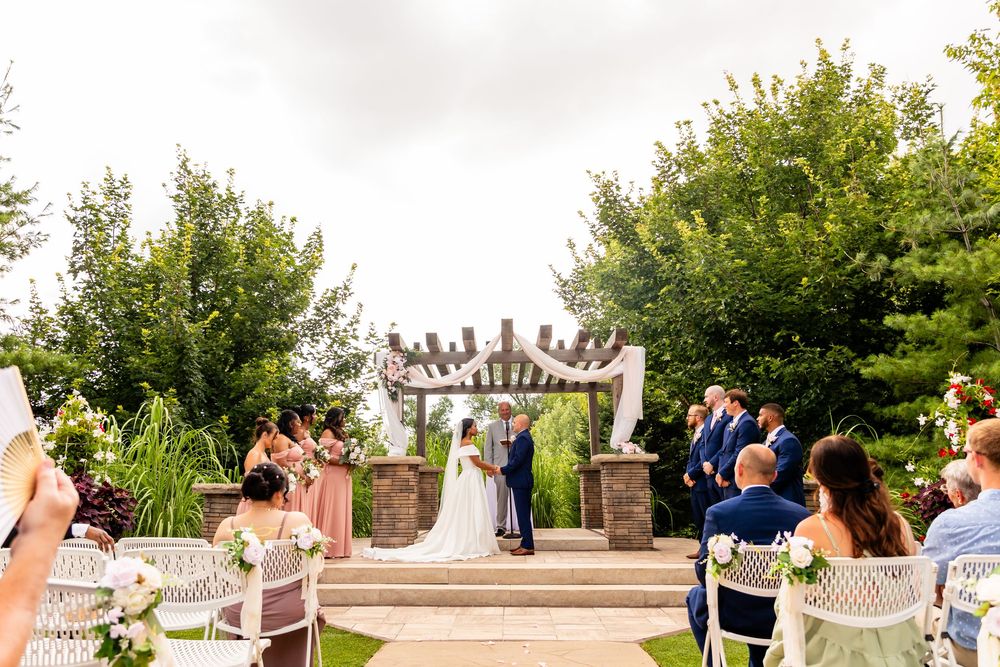Wedding party stands in formation on stone patio with lush greenery backdrop at Villa Aletta in Omaha, NE.