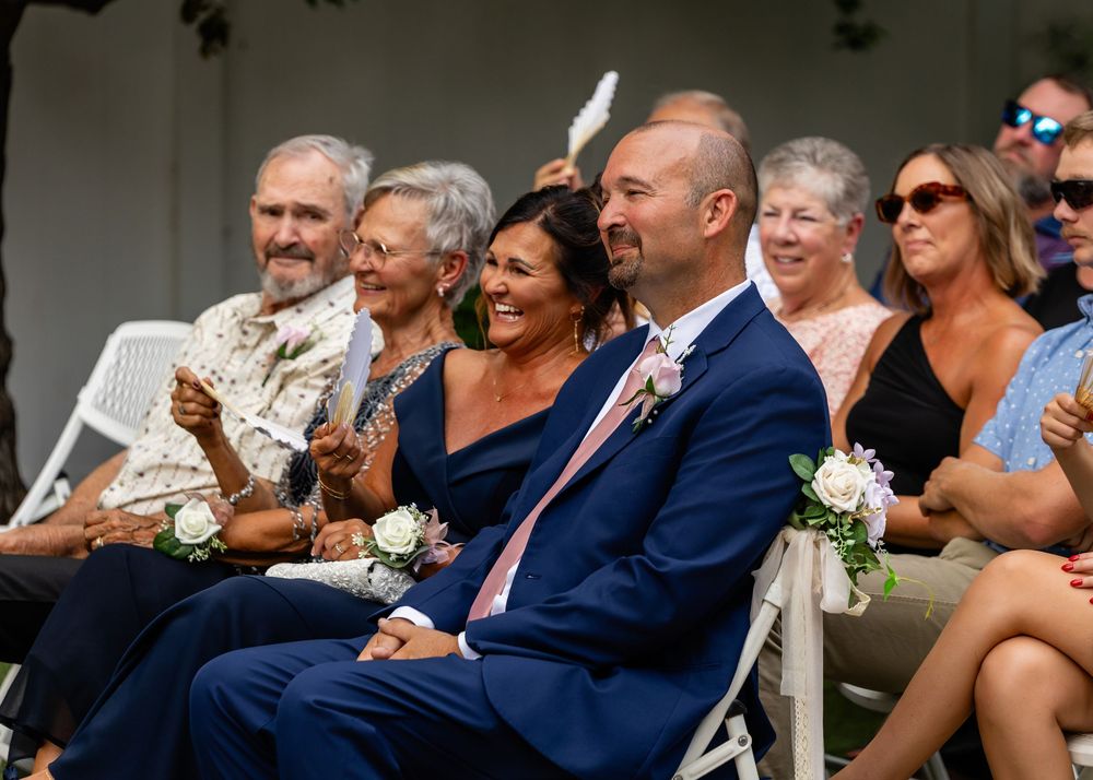 Wedding guests seated in white chairs watch ceremony with smiles and emotion.
