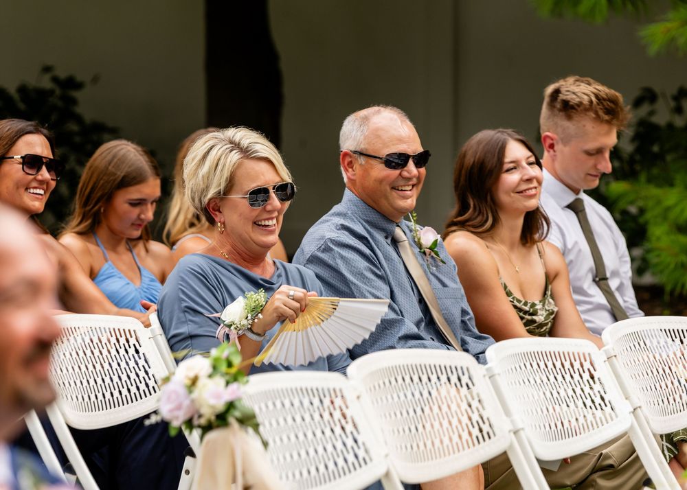 Wedding guests seated in white wicker chairs during outdoor ceremony.