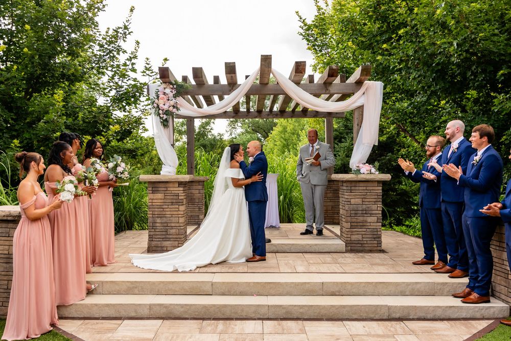 Wedding party and guests arranged on stone patio during outdoor ceremony at Villa Aletta in Omaha, NE.