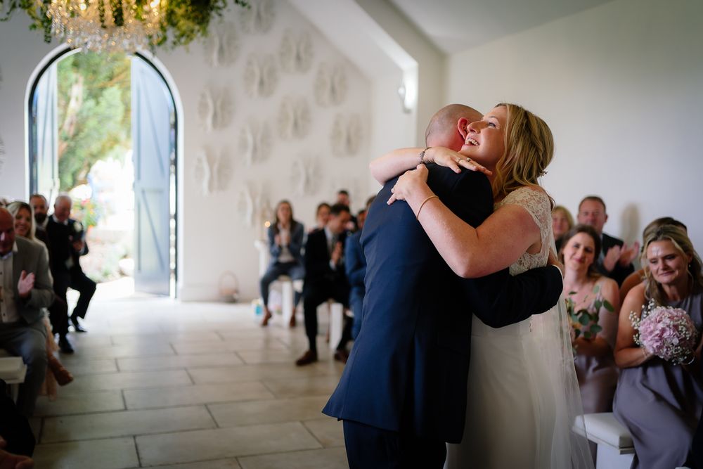 Wedding celebration moment captured in elegant white chapel interior. Woodhill Hall.