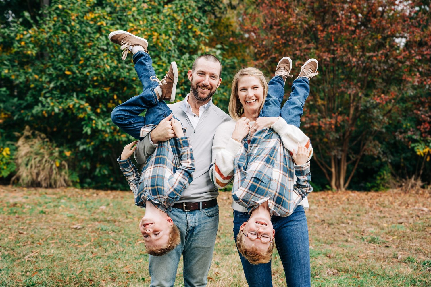 A family wearing coordinated blue and white outfits poses together in a fall outdoor setting for photos.
