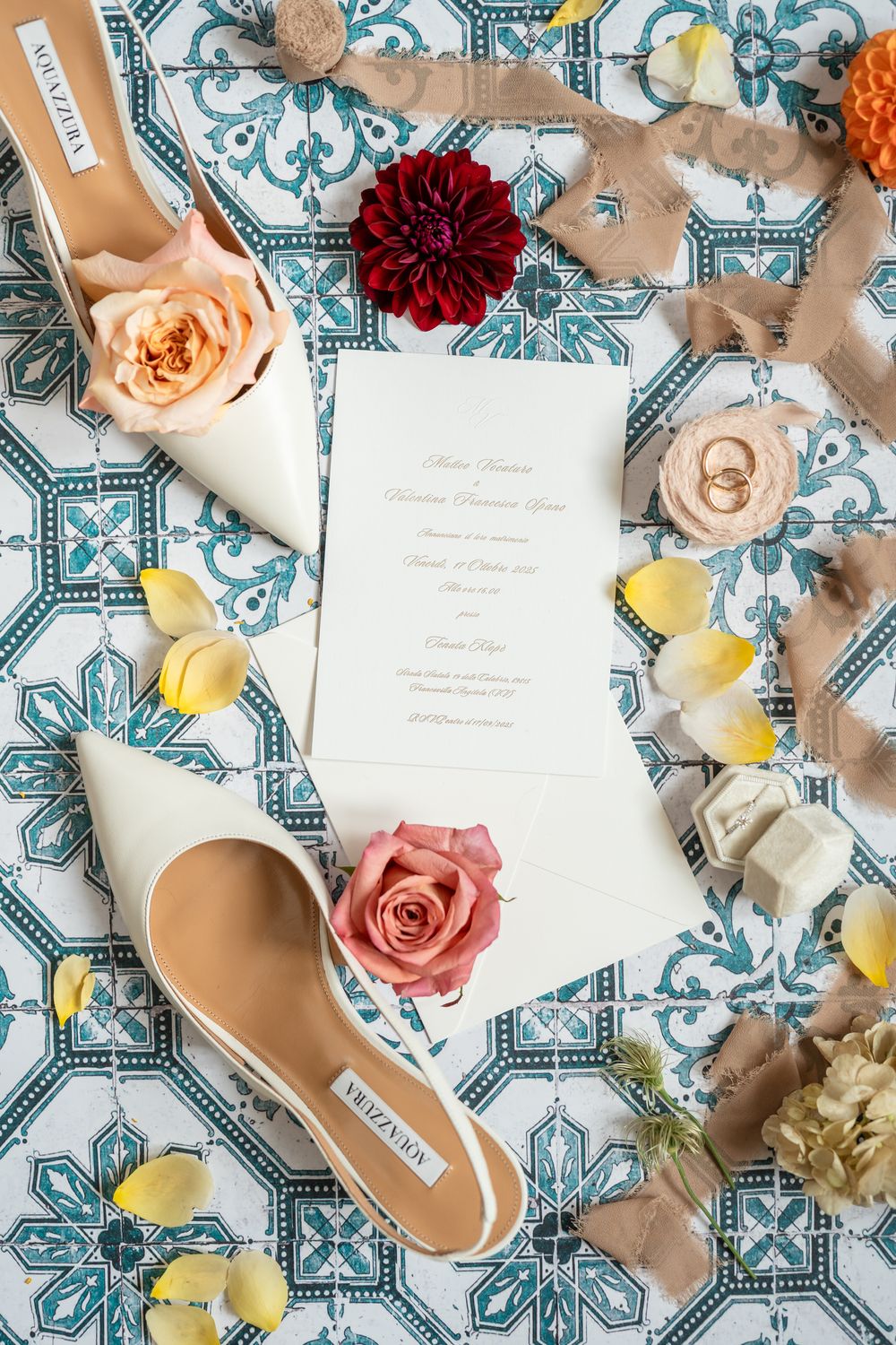 Wedding invitation cards and floral decorations arranged on blue and white patterned tile background with roses and dahlias.