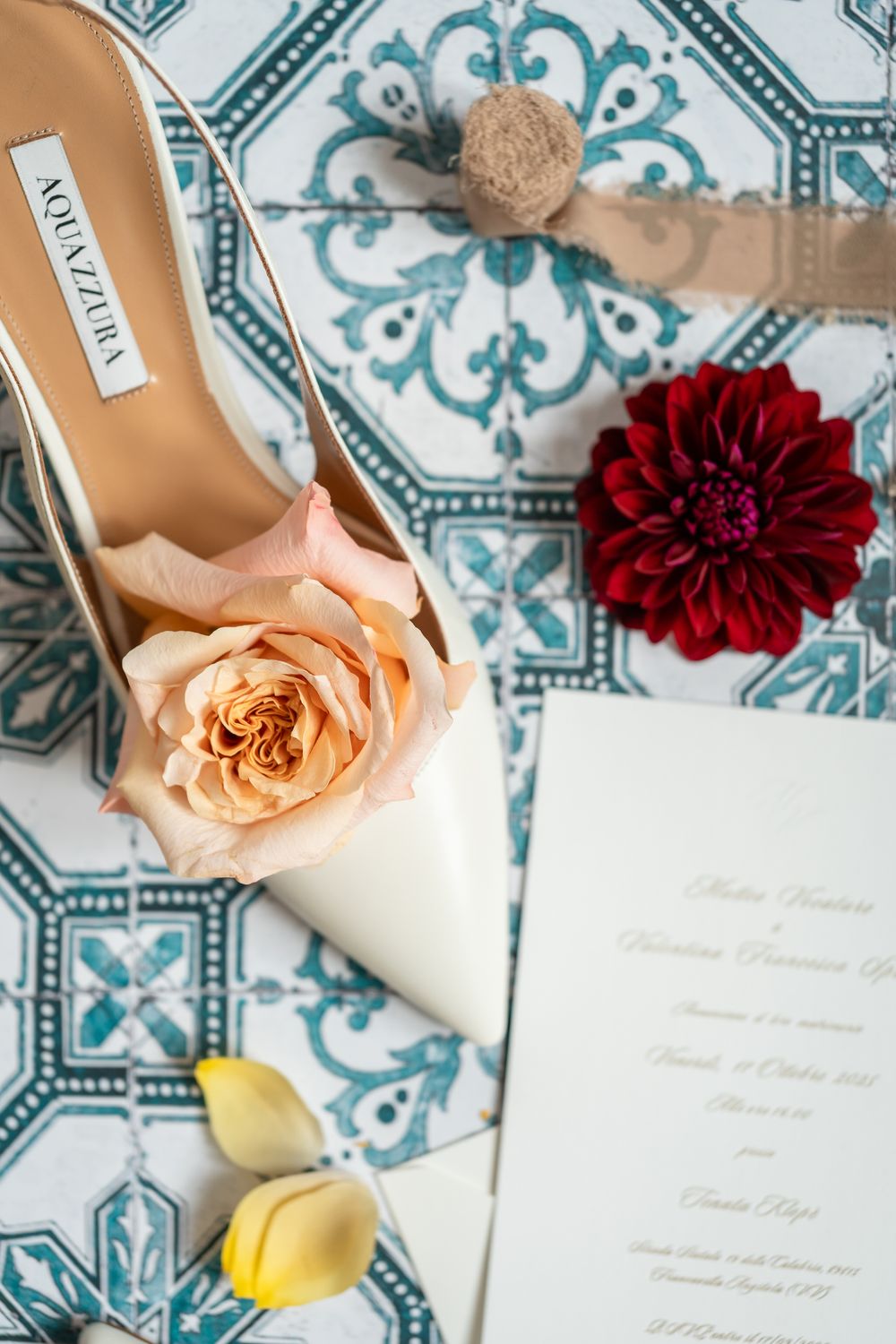 Wedding details featuring peach and red flowers with invitation cards laid on a blue and white patterned tile background.