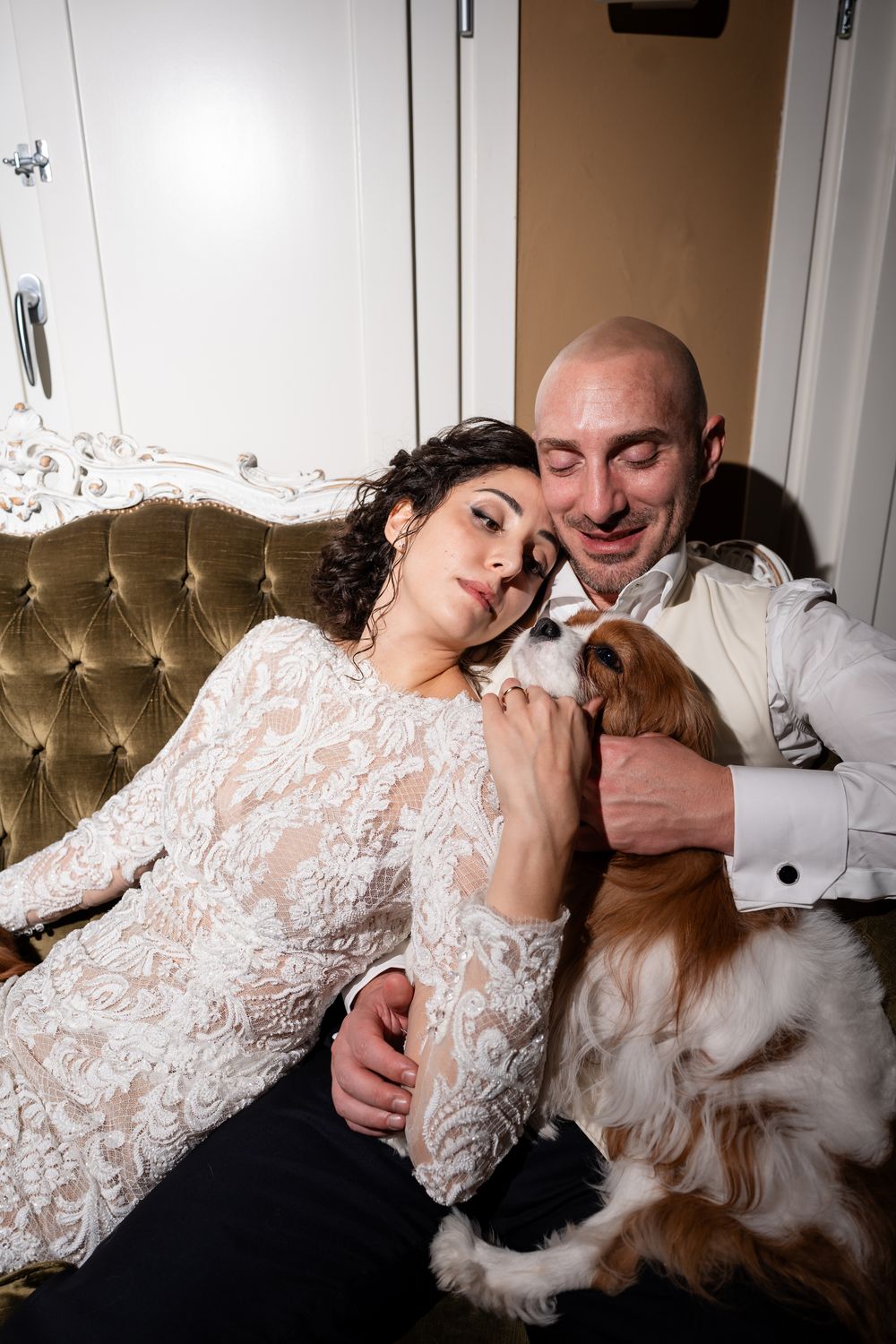 A couple relaxes on a tufted couch with their fluffy white dog in a series of sweet candid moments.