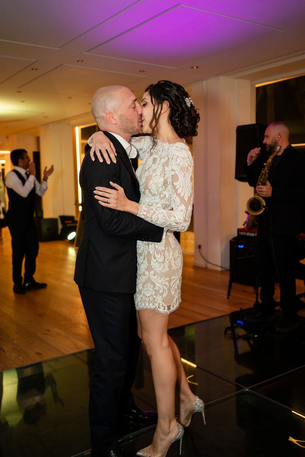Couples dancing together at an indoor event venue with purple lighting and wooden floors.
