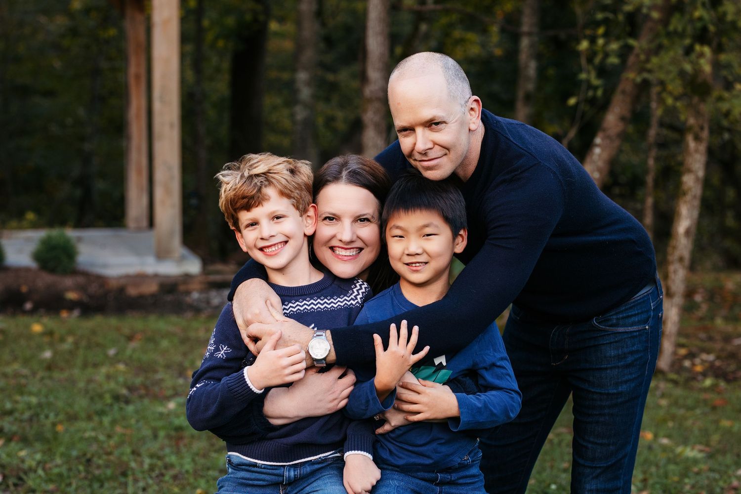 A happy family enjoying playful moments together outdoors in a wooded setting during autumn.