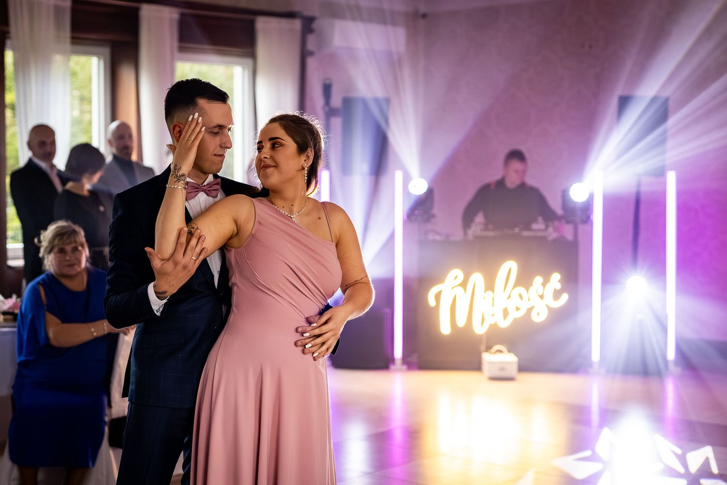 Couples dancing at a wedding reception with colorful lighting and neon signs in the background.