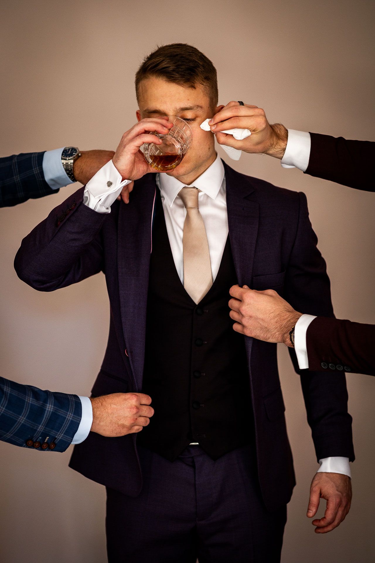 Groomsmen help adjust the groom's suit and tie in preparation for the ceremony.