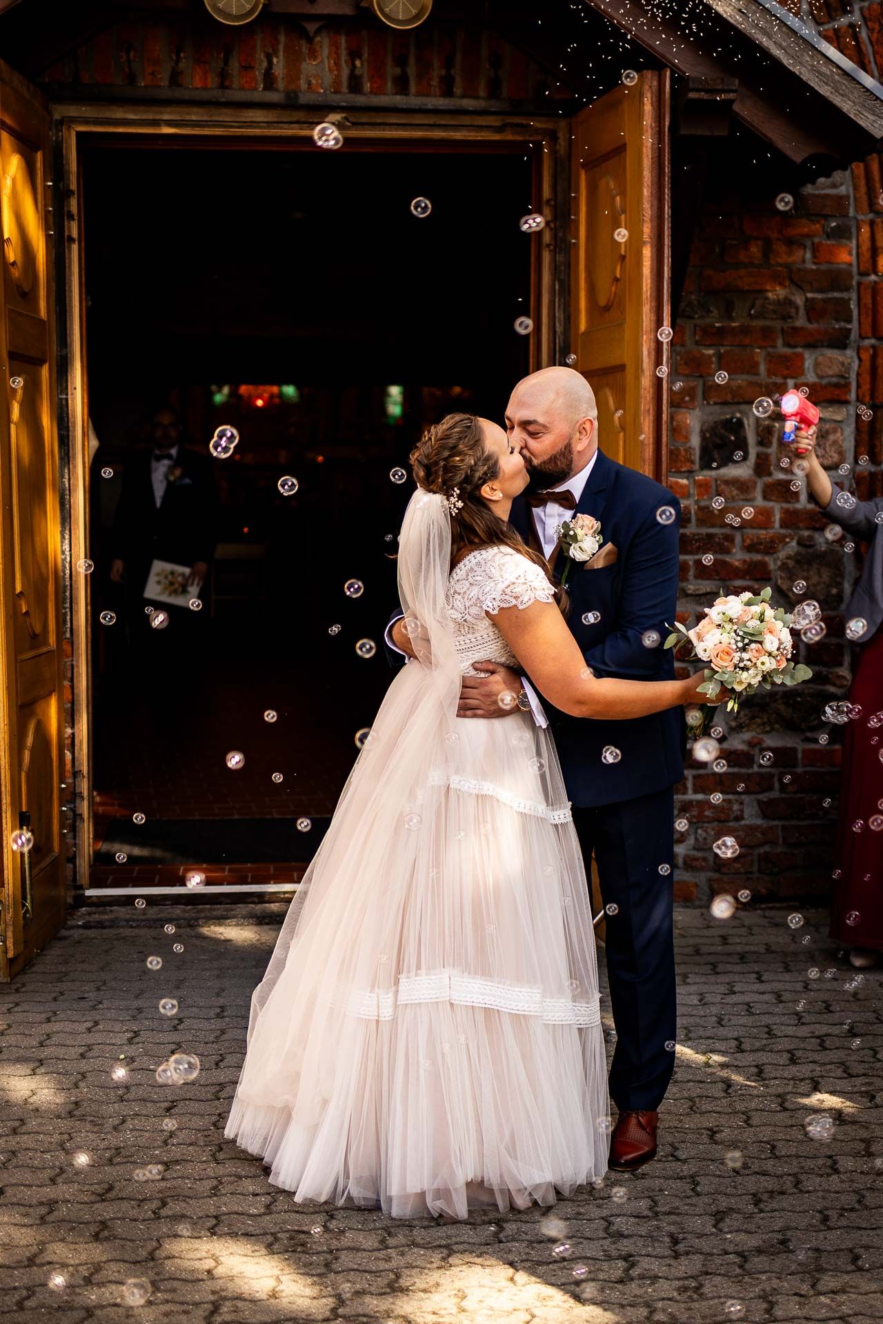 Newlyweds dancing surrounded by bubbles on cobblestone courtyard.
