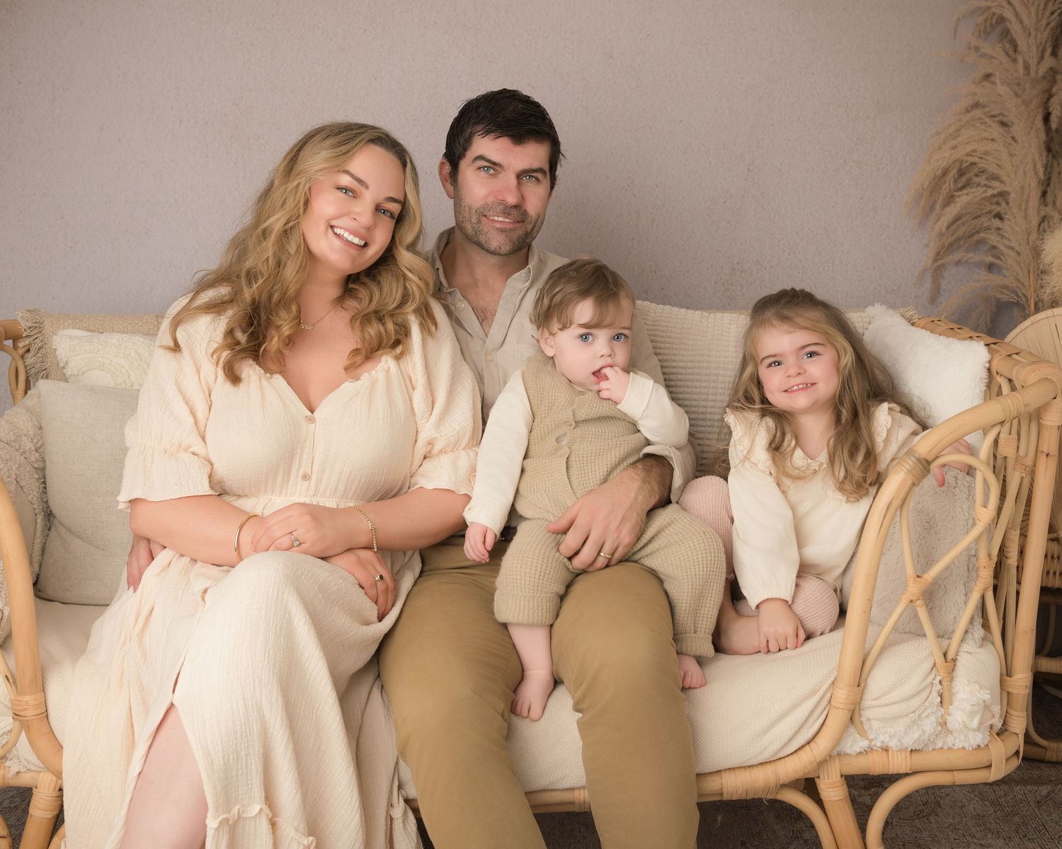 A family wearing coordinated cream and beige outfits poses together for a series of professional studio portraits.