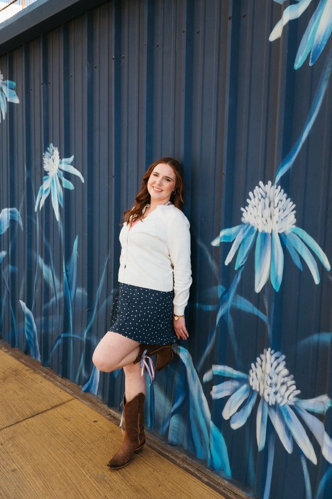 A white sweater and polka dot skirt outfit photographed against a blue wall with painted white daisy murals.
