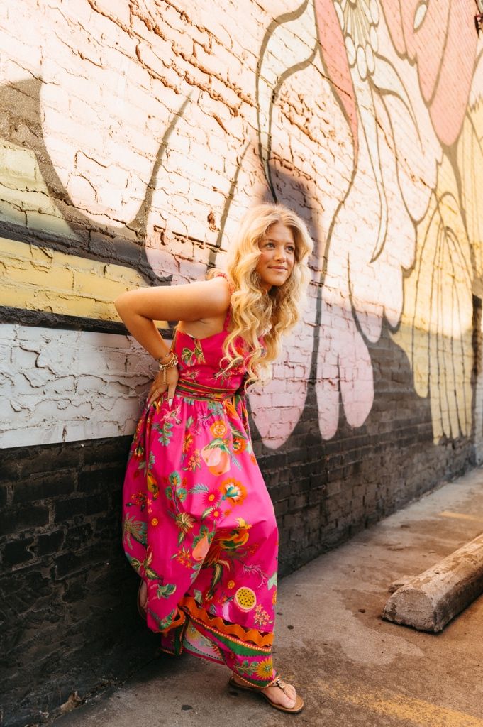 A child in a bright pink floral dress twirls playfully against a graffiti-covered brick wall.