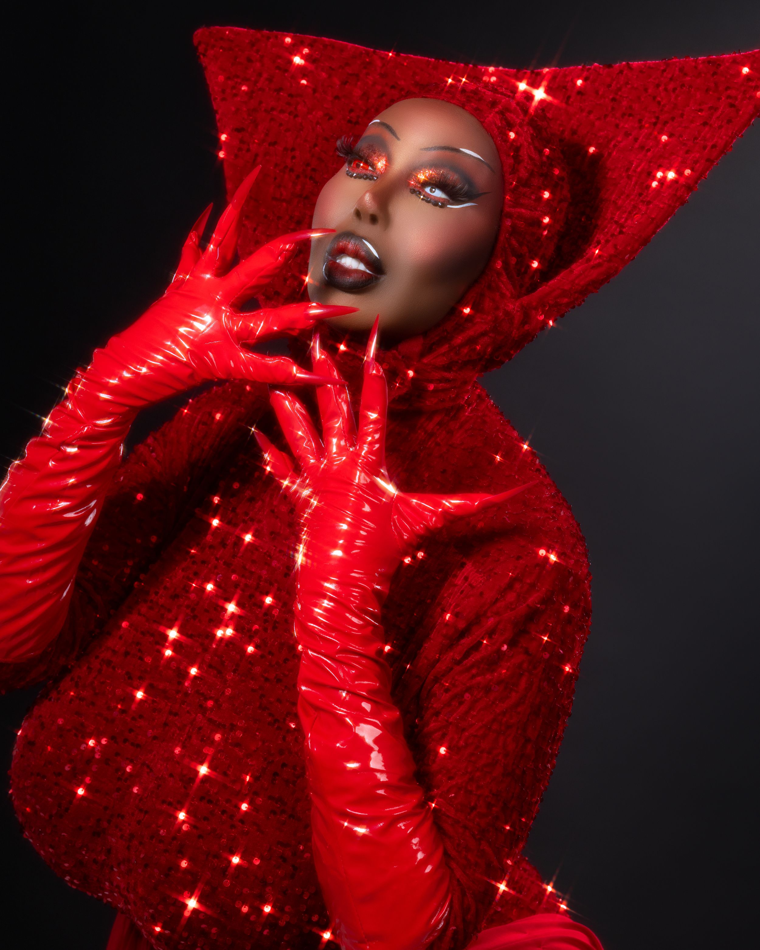 Fashion portrait in vibrant red featuring dramatic high collar and glittering sparkle effects against dark background.