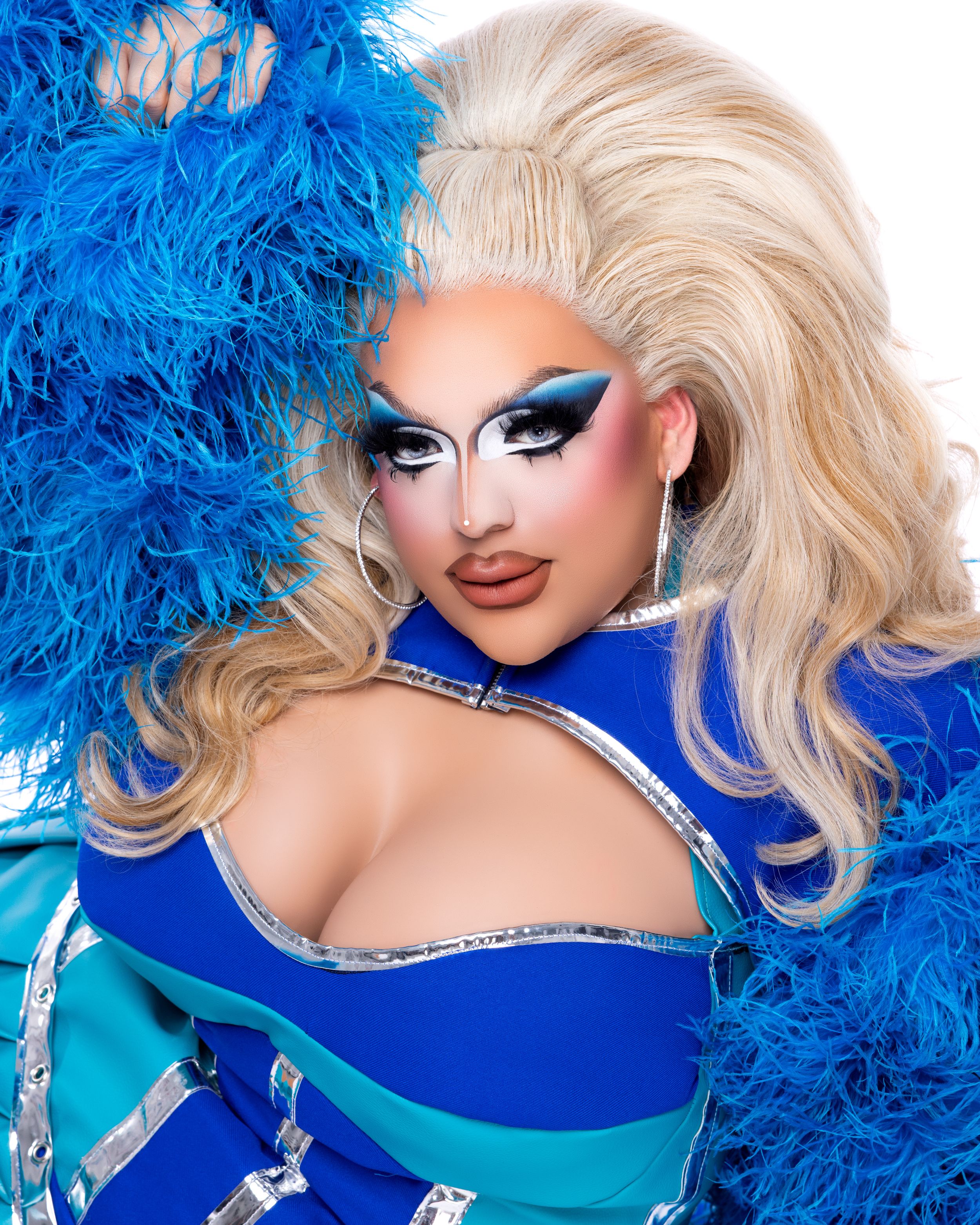 Glamorous drag performer in a royal blue sequined outfit with bright blue feather accessories and dramatic makeup.