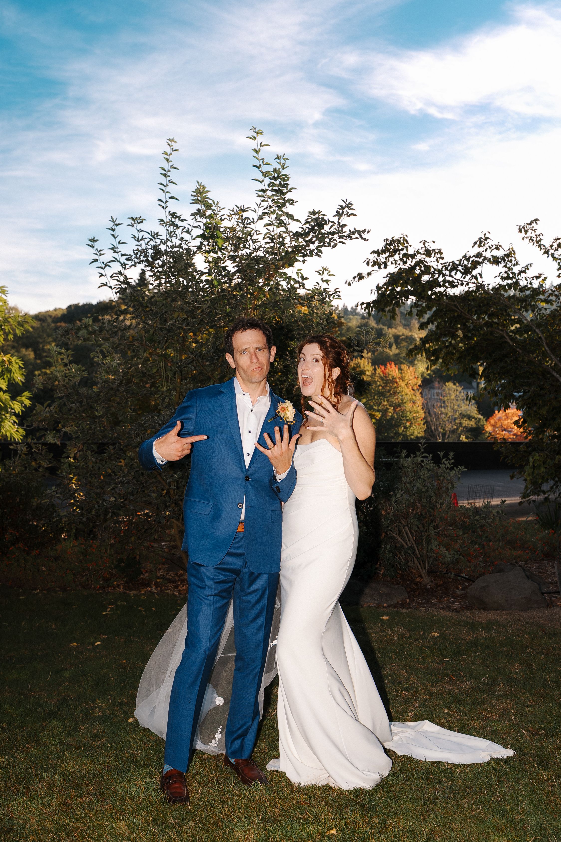 A couple in wedding attire shares a candid playful moment together in an outdoor garden setting at sunset.