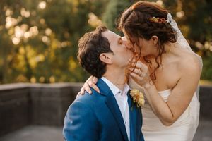 A romantic wedding couple shares tender kisses in a golden sunset light while wearing formal attire.
