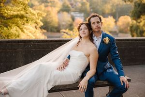 Couple sits together on rustic stone wall during golden hour wedding photoshoot.