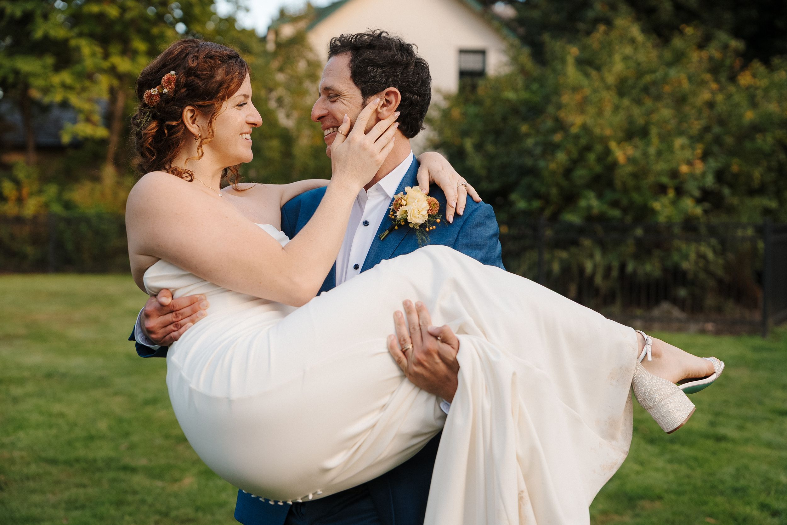 A couple shares a romantic moment in their wedding attire while dancing outdoors on a grassy lawn.