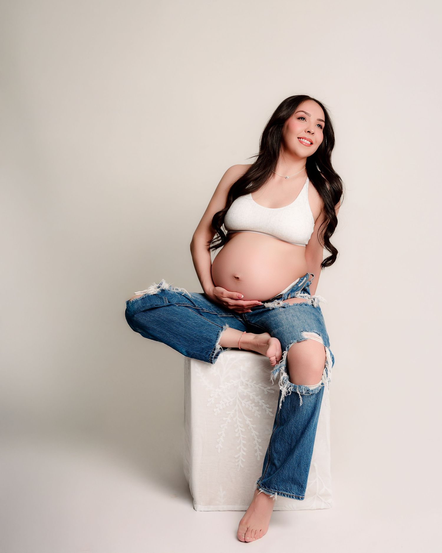 A series of maternity photos showing a pregnant woman in ripped jeans and white top posing against a light background.