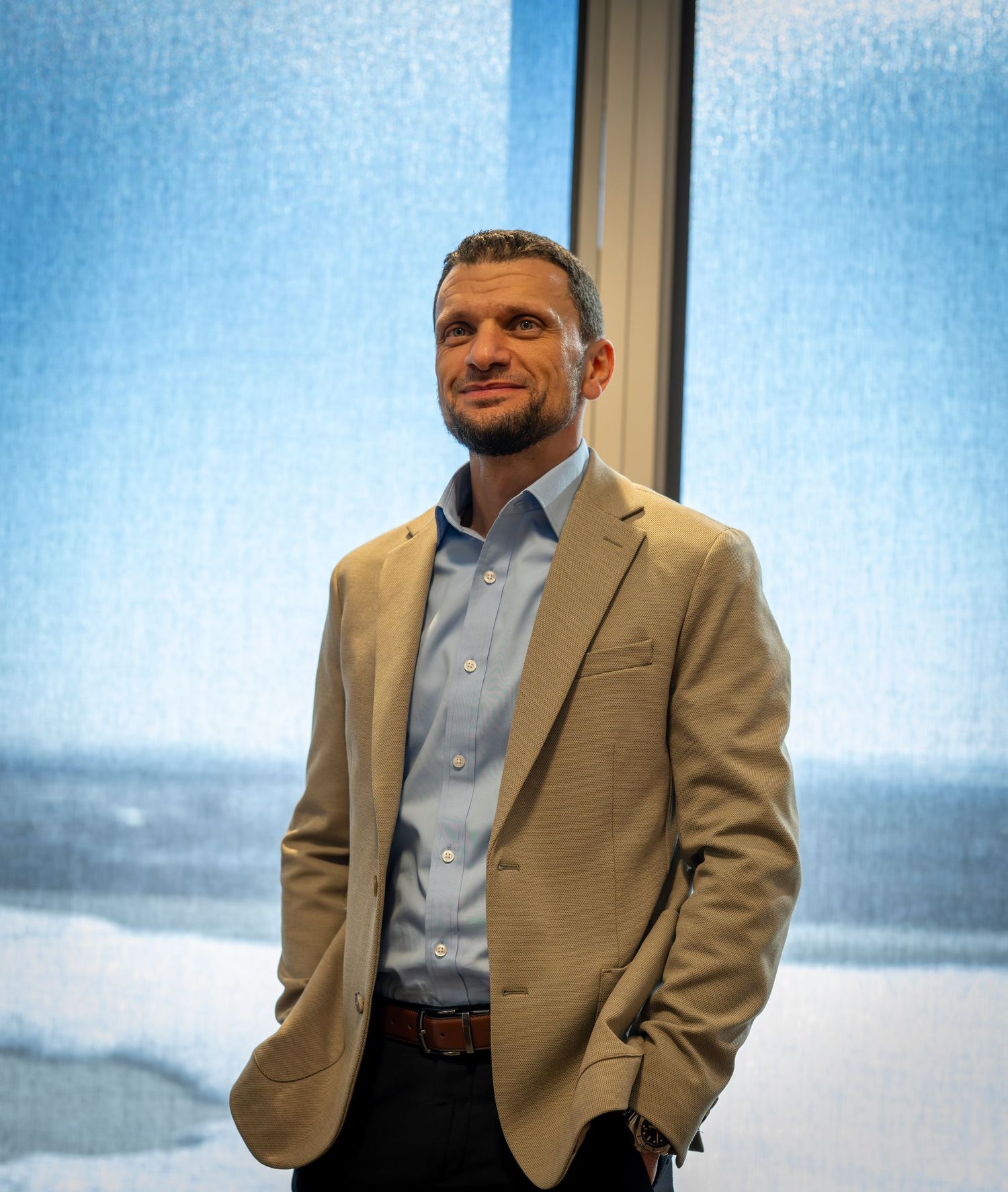 A person in a tan blazer and light blue shirt poses in a sequence of four similar photos against a light background.