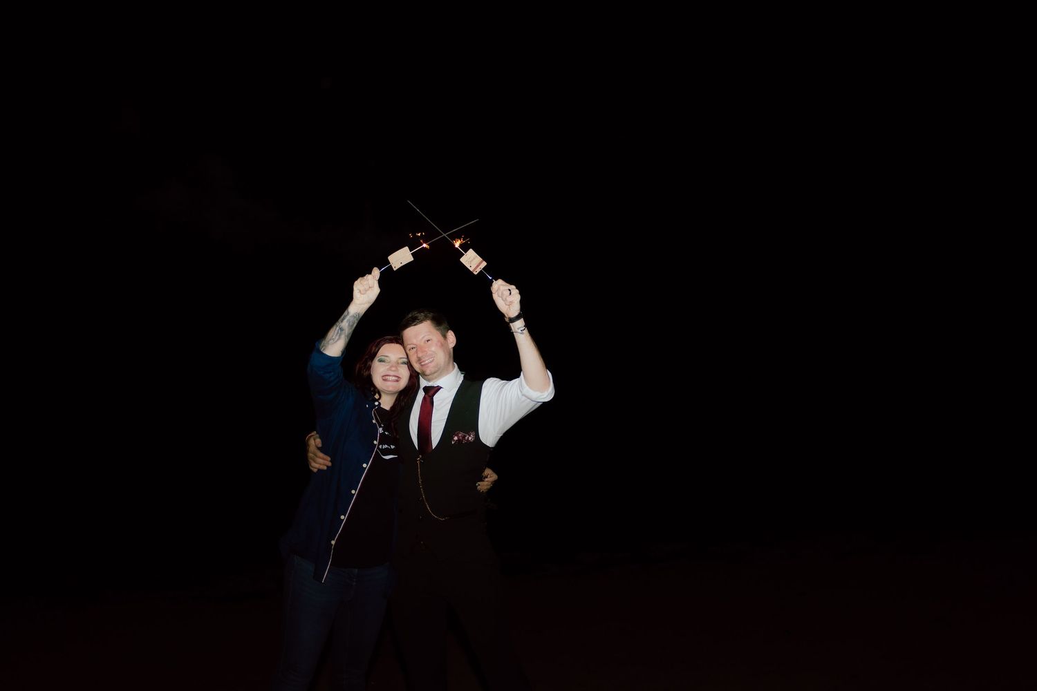 A couple dancing together in formal attire against a dark background, with arms raised in an elegant pose.