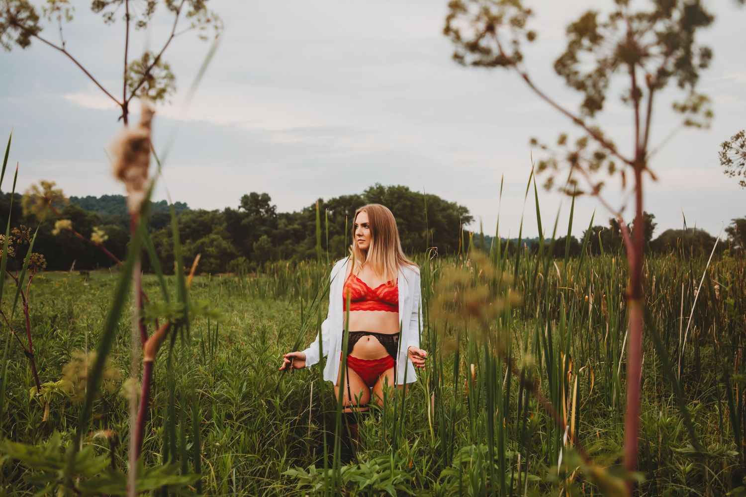 A person in red swimwear walks through a field of tall grass and wildflowers at sunset.