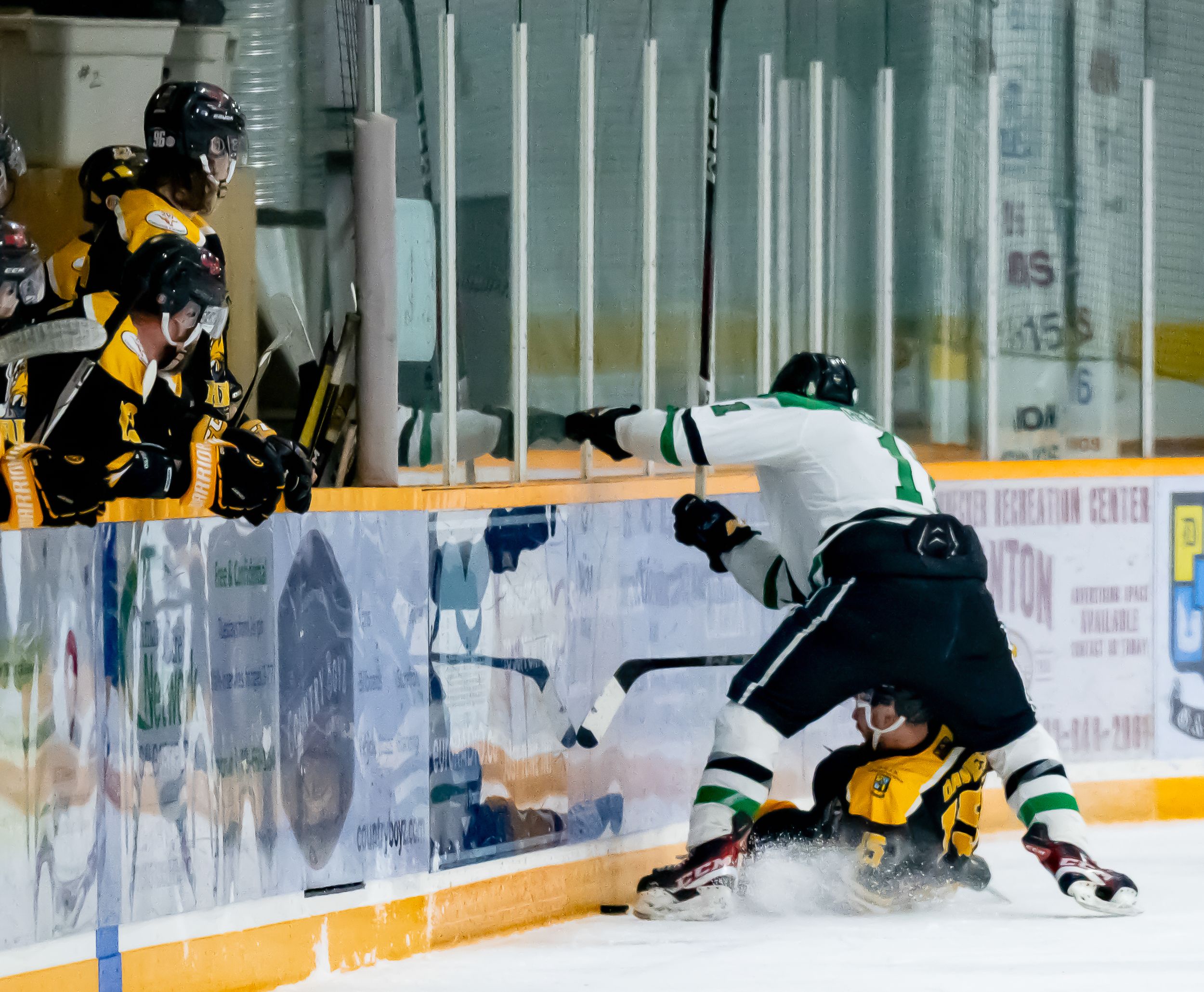 Hockey players in black and gold uniforms skate along the boards during a game.