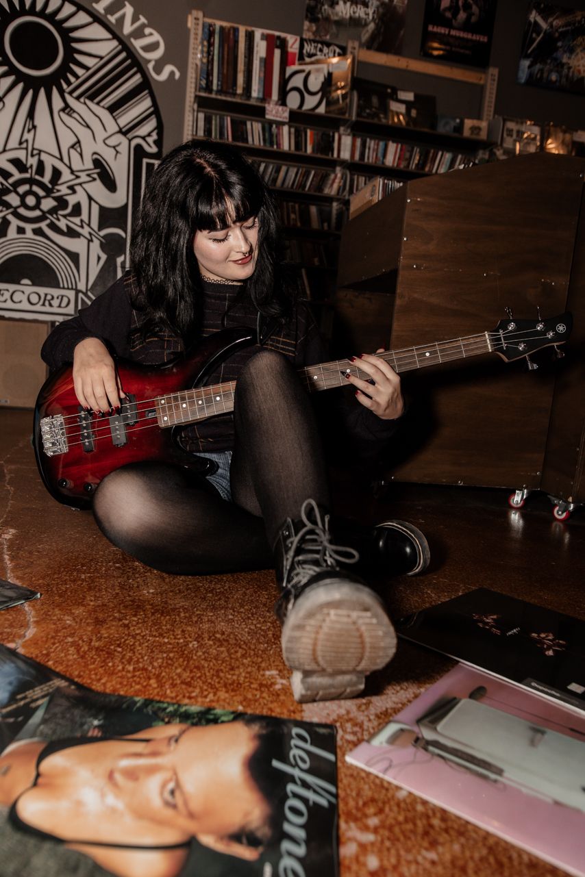 Person with guitar sitting on floor against wall decorated with artistic murals.
