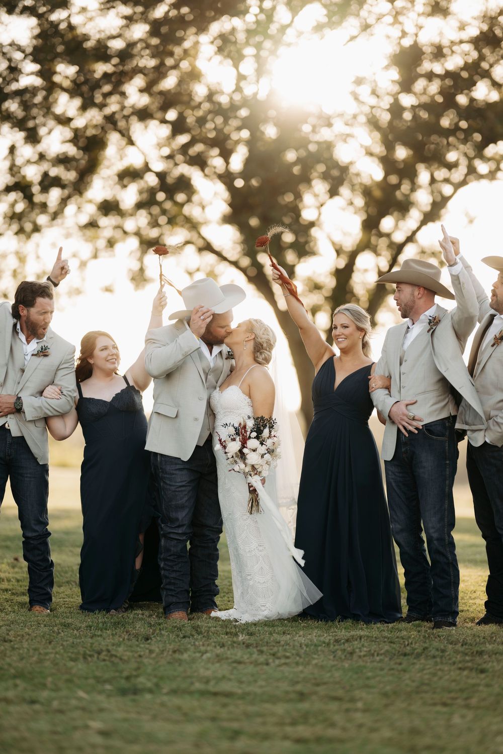 Wedding party in navy and white attire poses together at sunset in a grassy field.