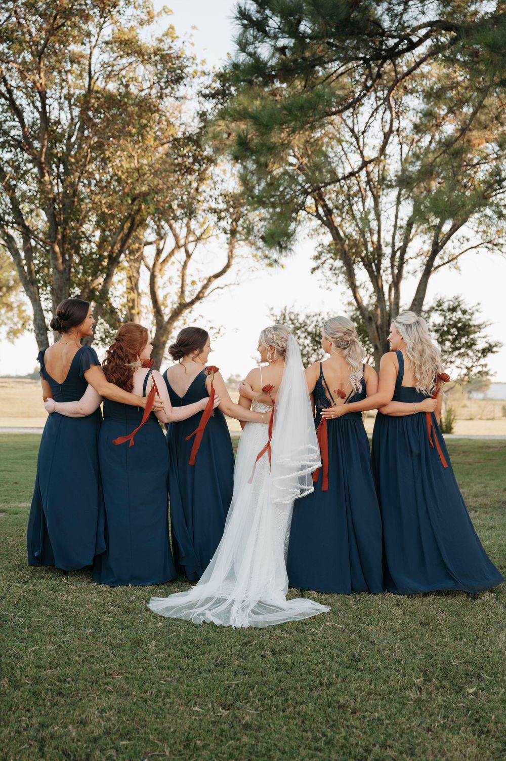 Wedding party in navy blue dresses and white gown posing together on grassy hillside.