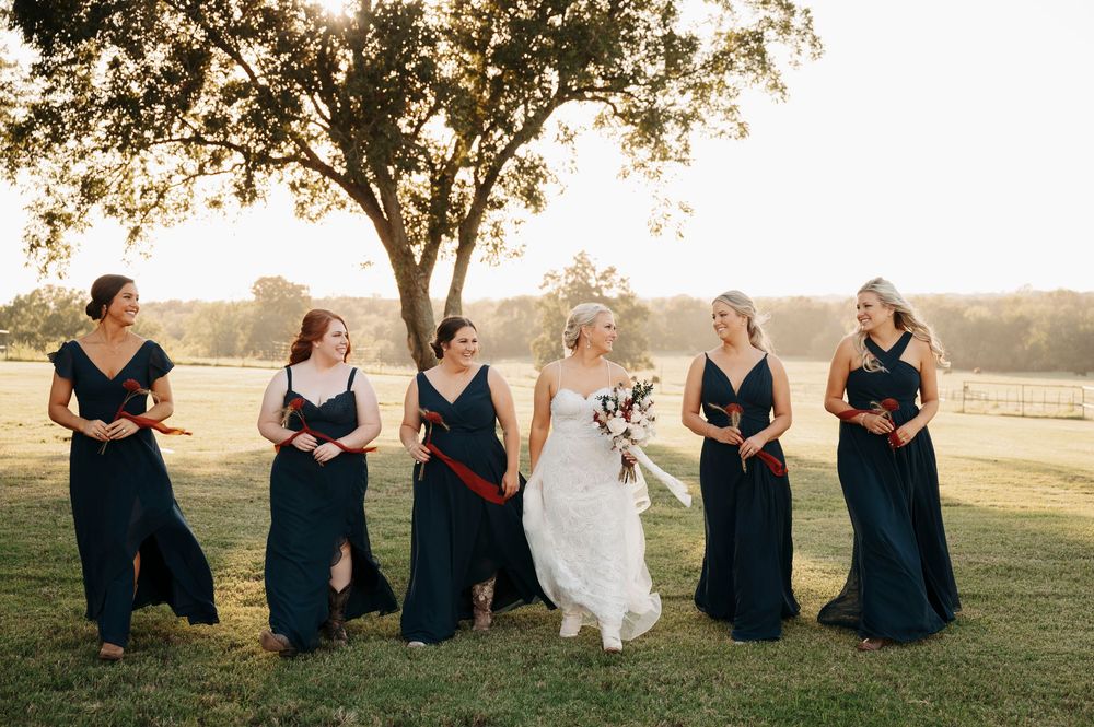 Wedding party in navy blue dresses sitting outdoors in a grassy field.