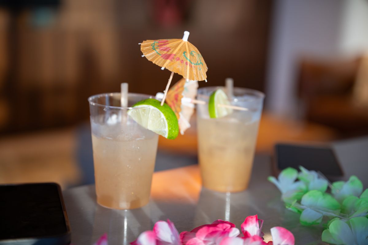 Tropical cocktails with umbrellas garnished with citrus and fresh herbs line up at an elegant bar.